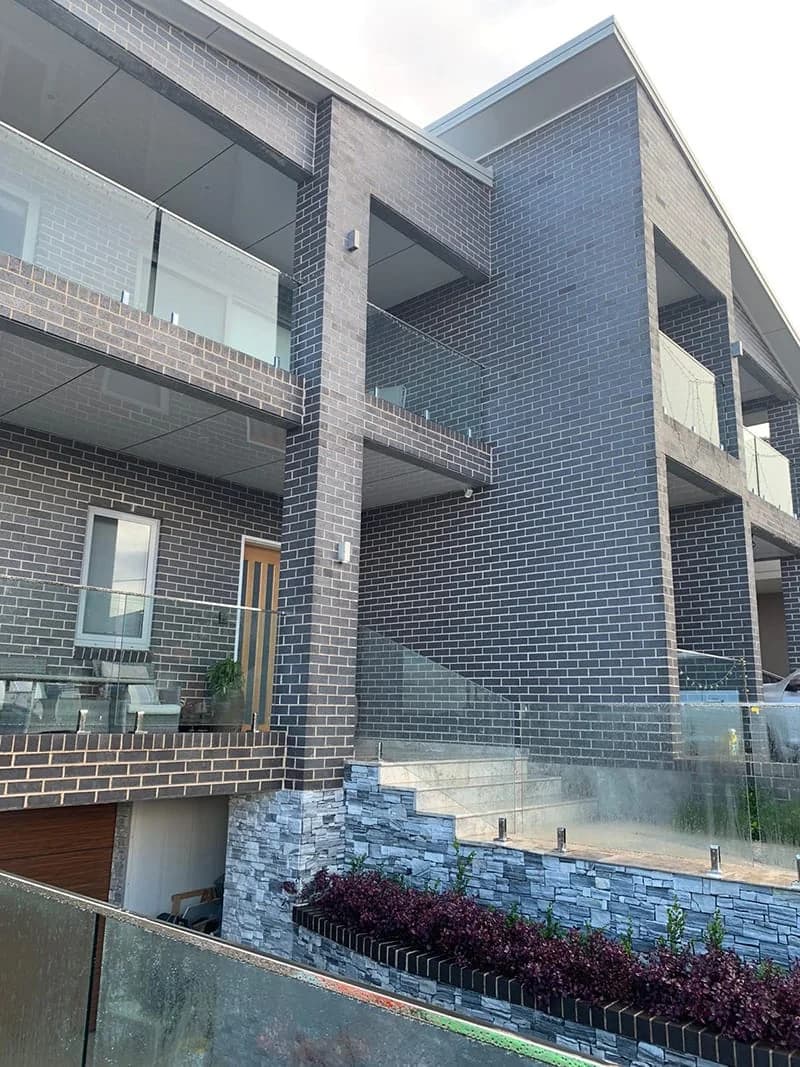 Modern dark brick townhouse with glass balcony details